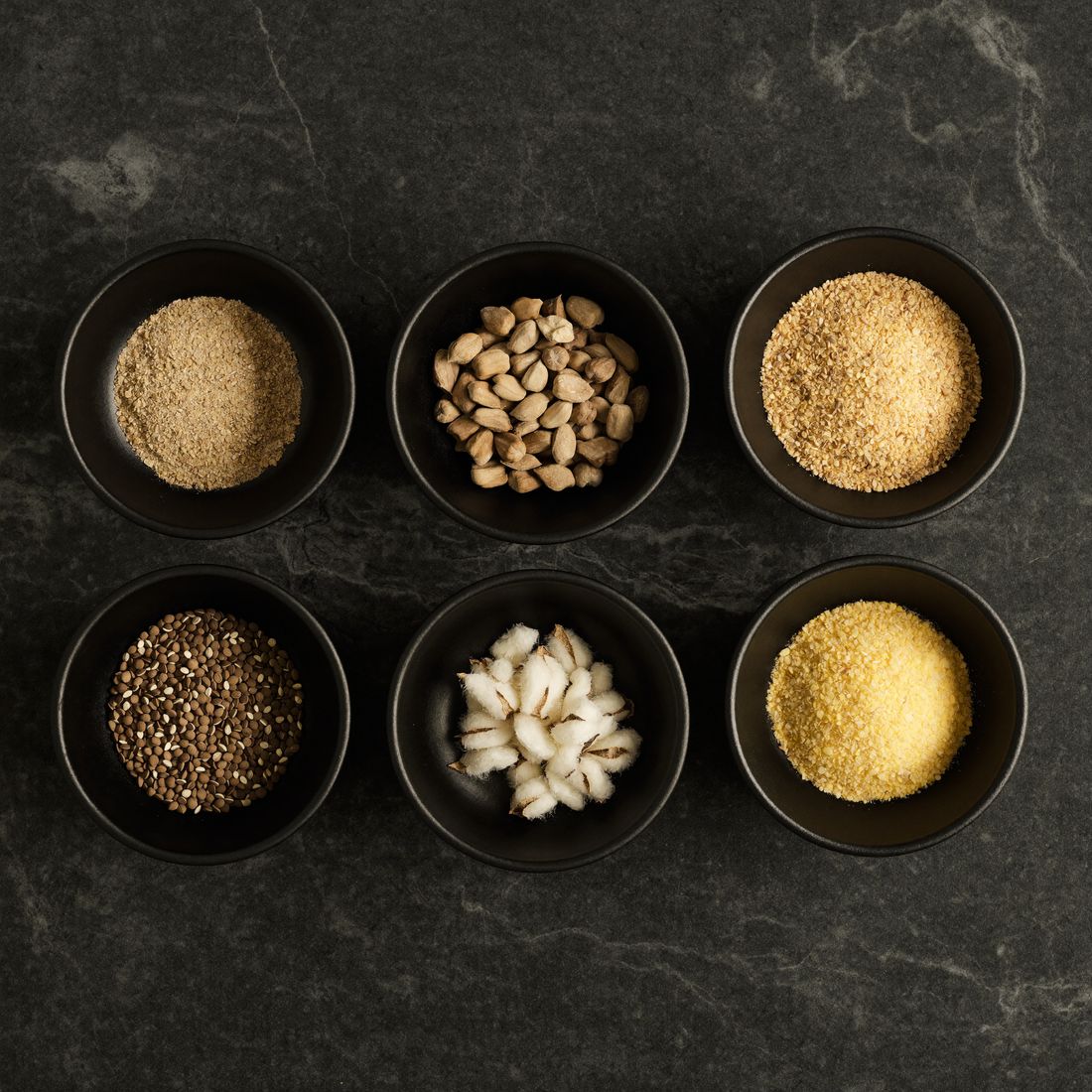 Sample bowls of bran, meal, seed and maize on dark stone